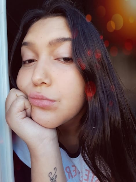 A close-up photograph showcasing the serene facial expression of a young Asian woman. She is an actress from an upcoming South Korean action dorama set to make waves in 2025. She stands out because of being extremely focused, determined, and filled with emotions, with soft lighting emphasizing the warmth and sincerity in her expression. She is featured in an outdoor scenic background, enhancing her natural beauty.