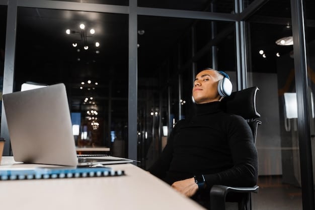 A person in a modern office with headphones listening to stream music in the middle of a busy office, where other people work in the background.
